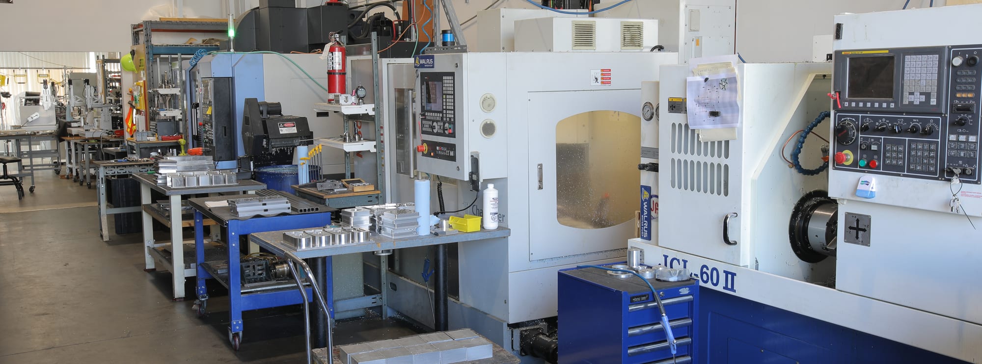 The NS CNC machine shop floor: mills and a lathe alongside benches of machined parts
