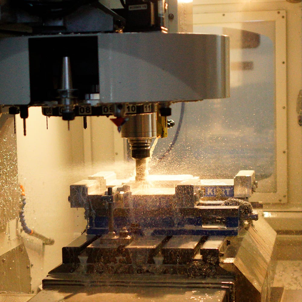 A vertical machining center milling a part held in a Kurt vise, chips and coolant spraying