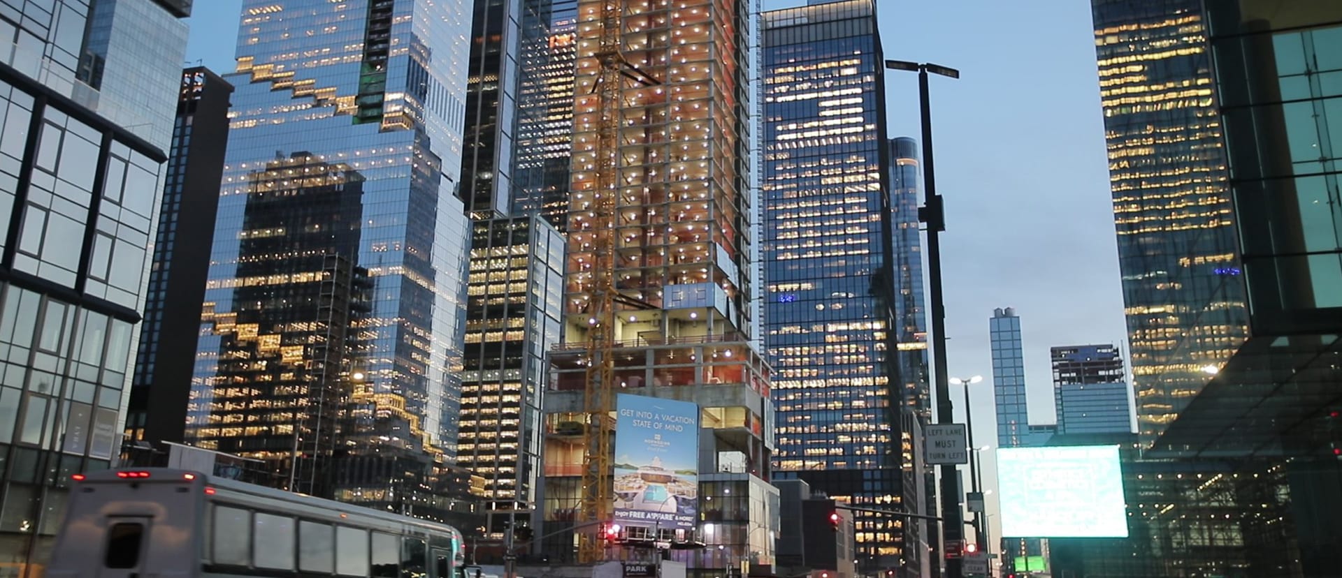 Glass office towers lit up at dusk along a busy city street
