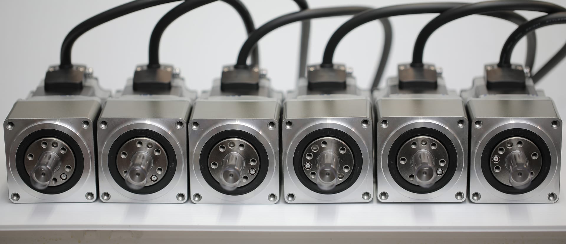 A row of six servo motors with their cables, lined up on a bench