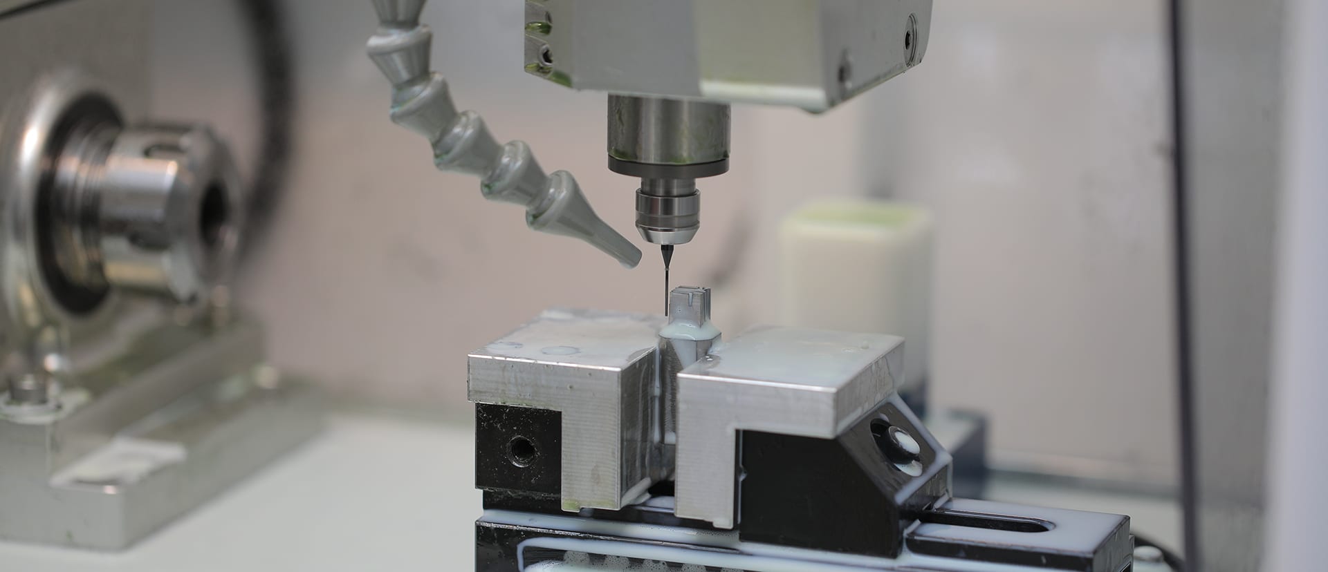A micro end mill cutting a small part held in a vise, under coolant