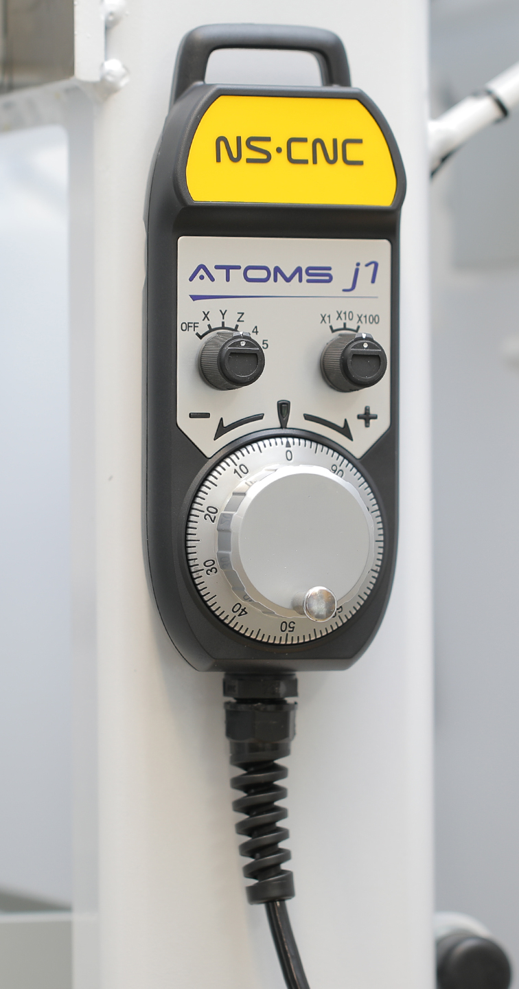 NS CNC branded handheld MPG pendant on a machine column, with an axis selector marked X, Y, Z, 4, 5, a step selector marked X1, X10, X100, and a graduated jog handwheel