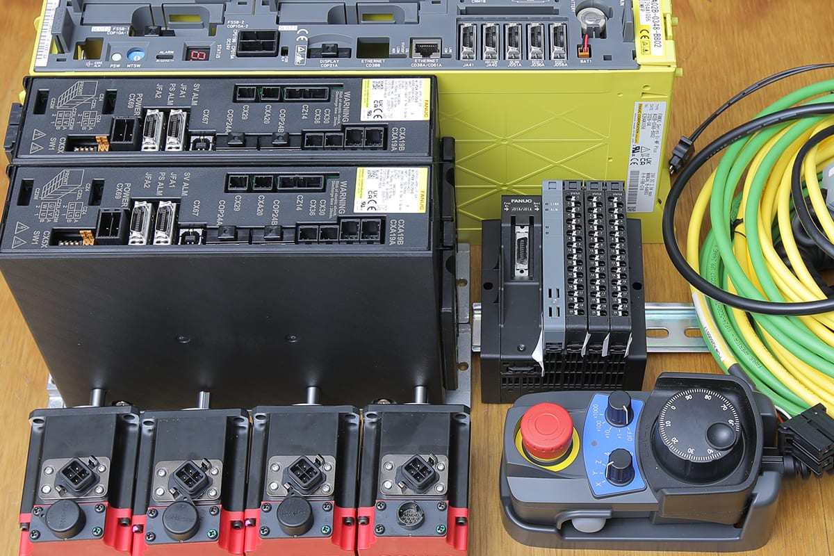 FANUC control components laid out on a bench: servo amplifiers, servo motors, an I/O module, cables, and a handheld MPG pendant