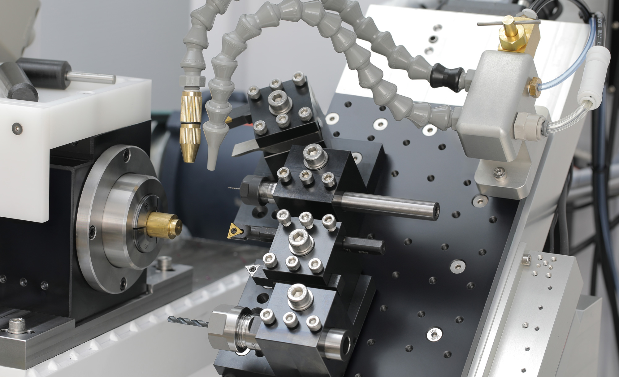 Tool posts fastened to the Lathe 3 X carriage table, with turning tools, drill holders, and coolant nozzles arranged around the spindle